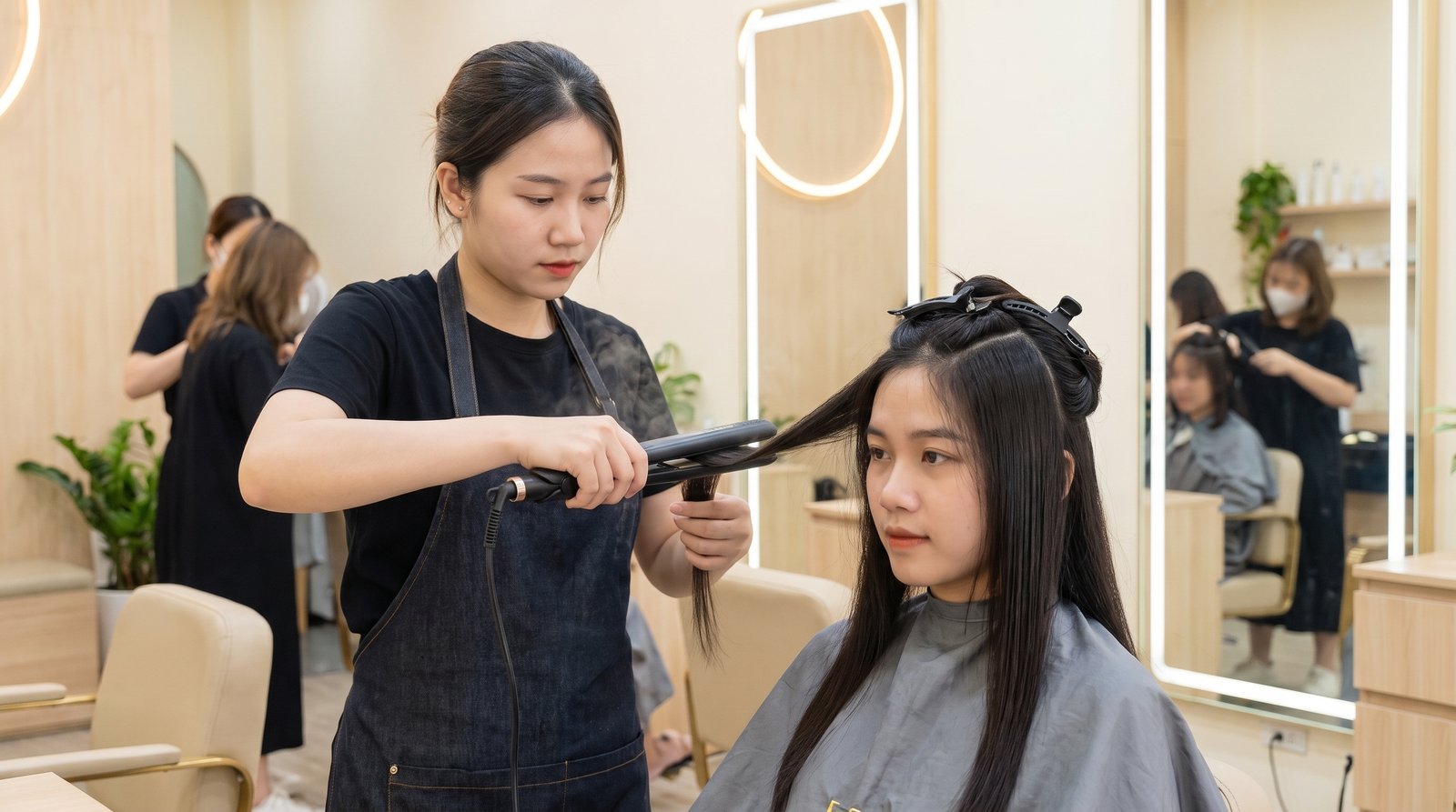 Thợ tóc duỗi ép từng lọn tóc bằng máy ép phẳng tại salon