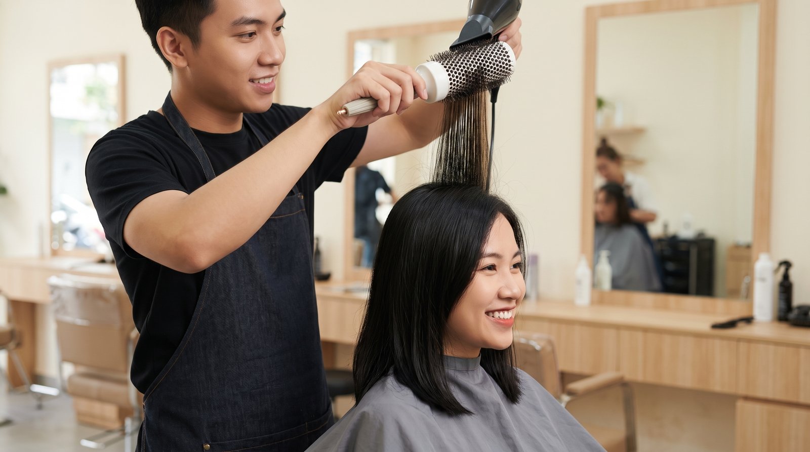 Thợ tóc dùng lược tròn và máy sấy nâng chân tóc tạo phồng tại salon